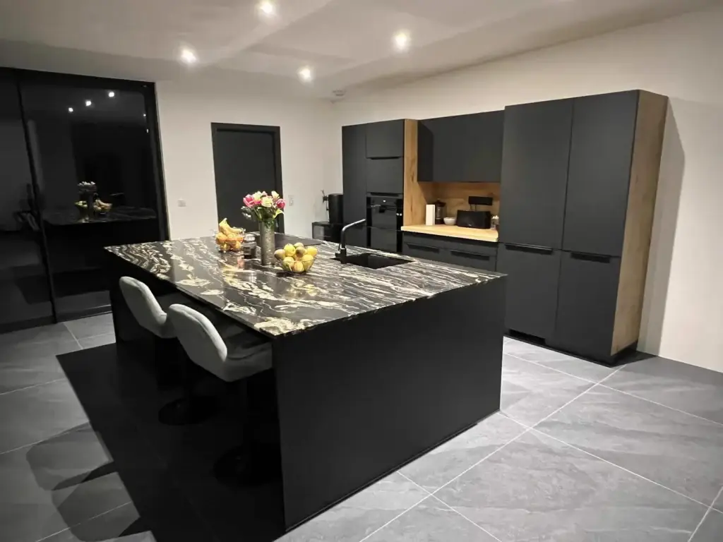 Cuisine noire mate avec îlot XXL et granit marbré doré à Châlonvillars